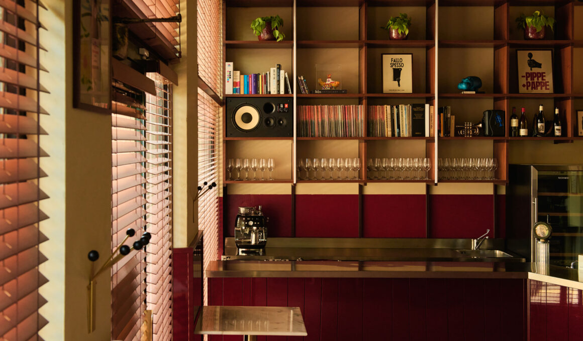 Interior of Nino Osteria in Milan featuring deep red wood paneling, a stainless steel bar counter, and built-in shelving with vinyl records and a speaker.