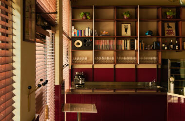 Interior of Nino Osteria in Milan featuring deep red wood paneling, a stainless steel bar counter, and built-in shelving with vinyl records and a speaker.