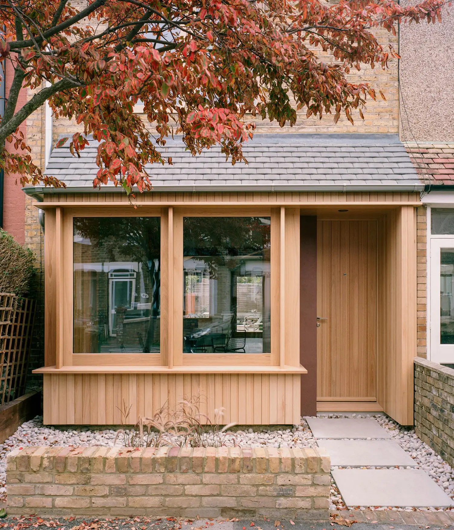 Close-up of a contemporary timber porch with a vertical wood-paneled door and large windows under a slate roof.