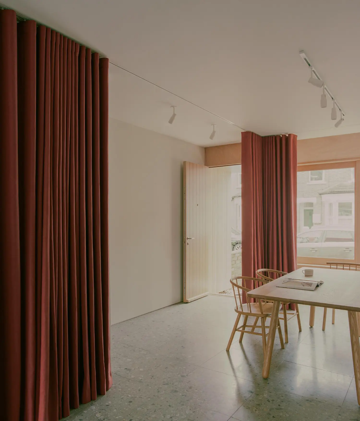 A dining space with a wooden table and chairs featuring a thick red curtain used as a flexible room divider.
