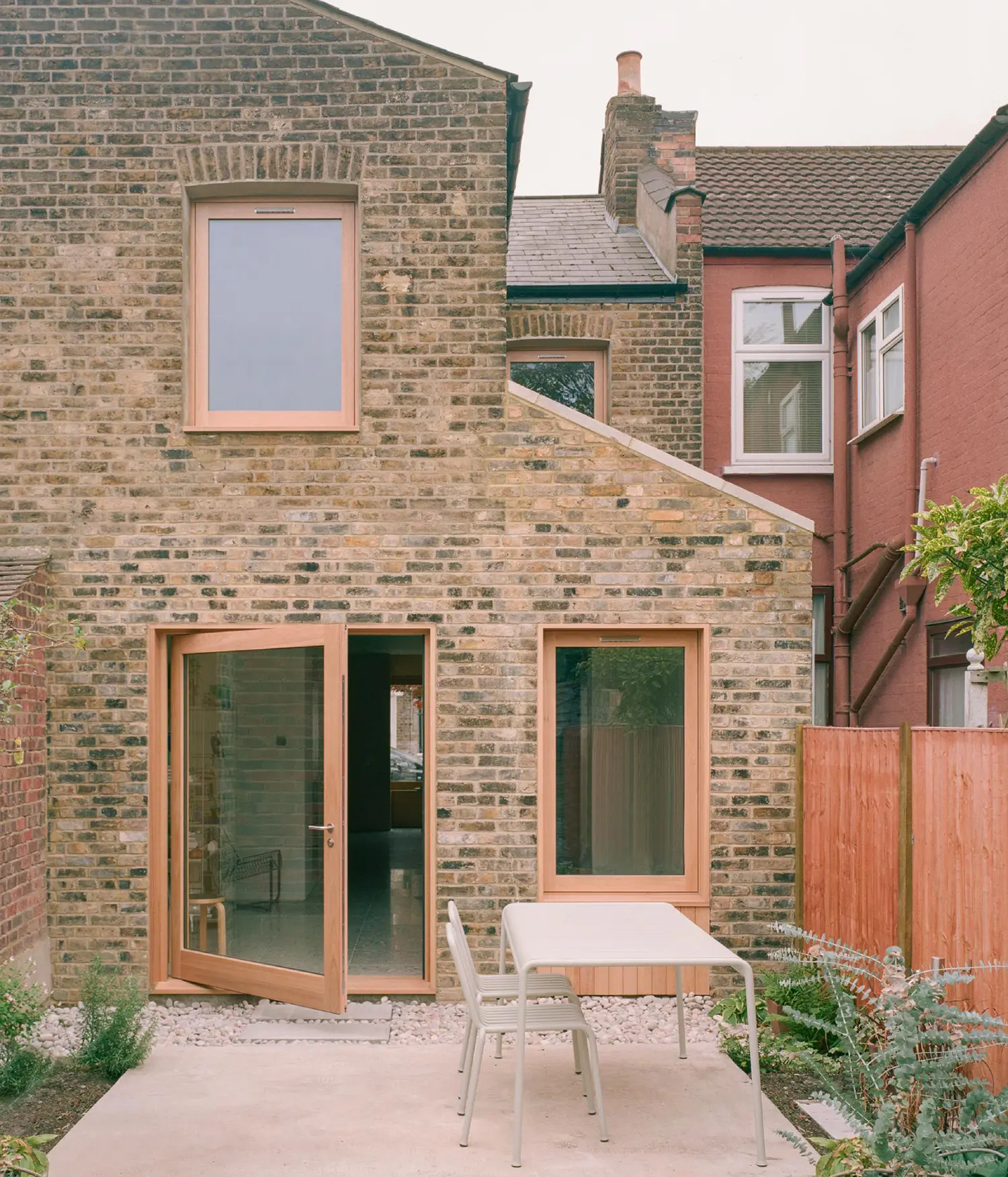 Rear view of a brick Victorian house extension with large timber-framed windows and a pivot glass door leading to a patio.
