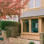 Exterior view of a Victorian house in Walthamstow featuring a contemporary Red Grandis timber porch and large glass windows.