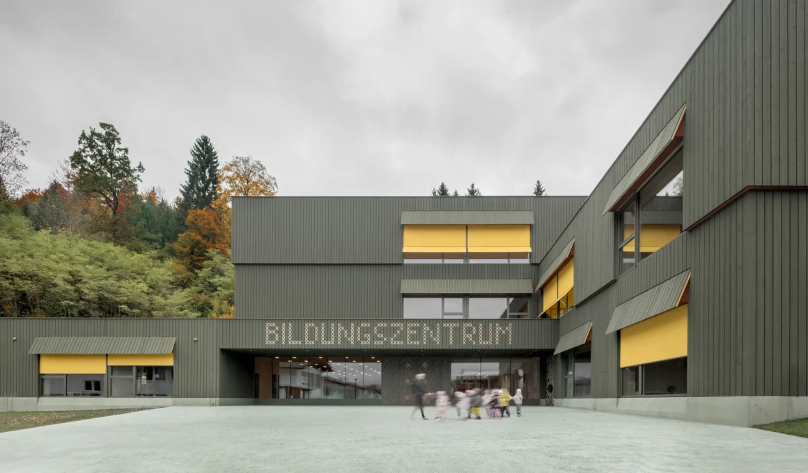 Education Centre Kössen by Pedevilla featuring green-stained wood facade and children in the central courtyard.