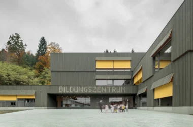Education Centre Kössen by Pedevilla featuring green-stained wood facade and children in the central courtyard.