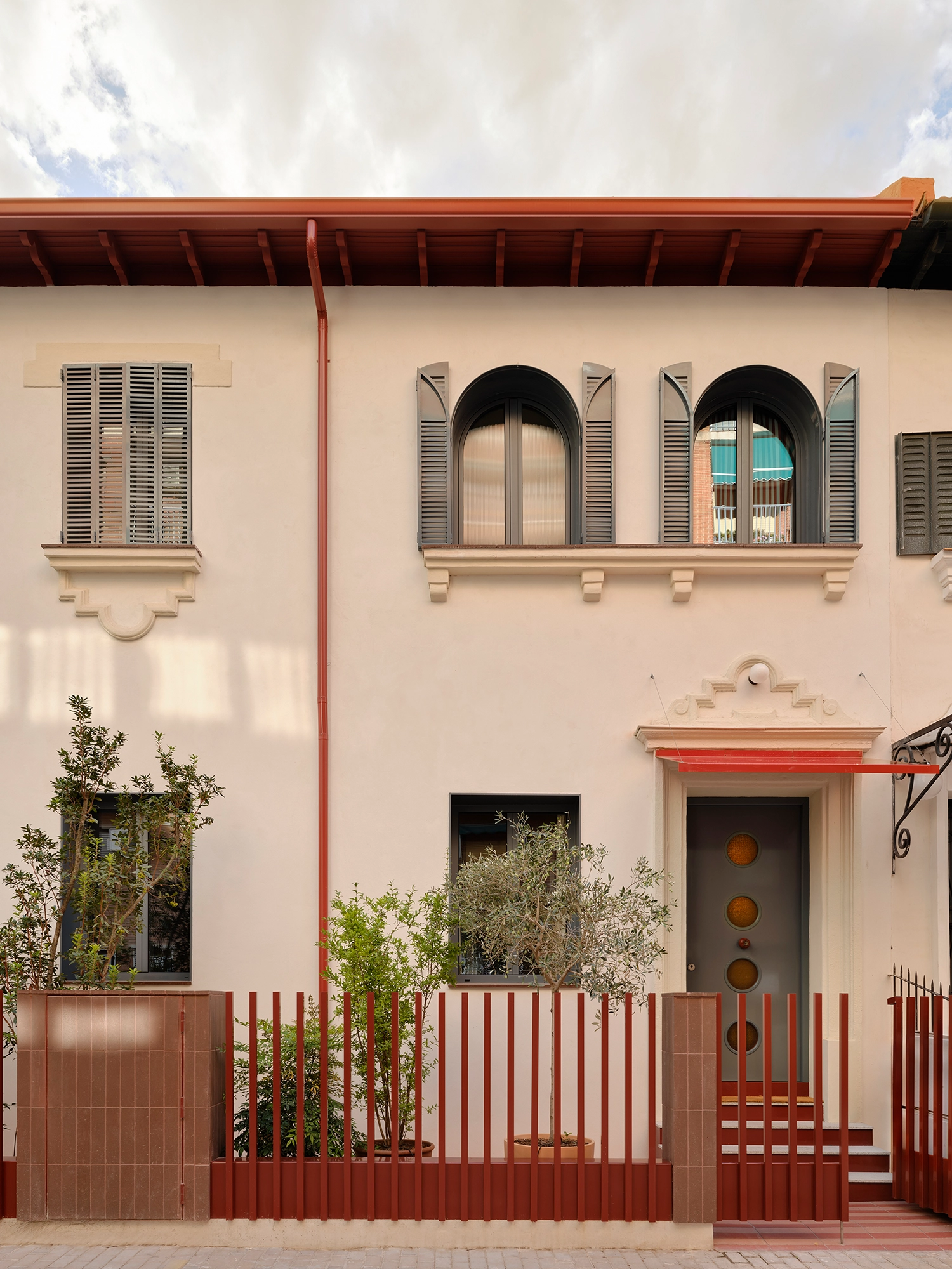 Exterior facade of a 1934 Madrid villa with arched windows, grey shutters, and a red metal fence.