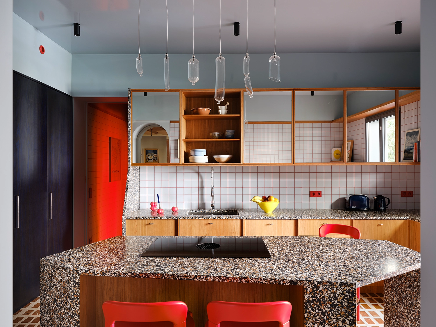Contemporary kitchen with a large terrazzo island, wooden cabinetry, and blue walls with red electrical sockets.