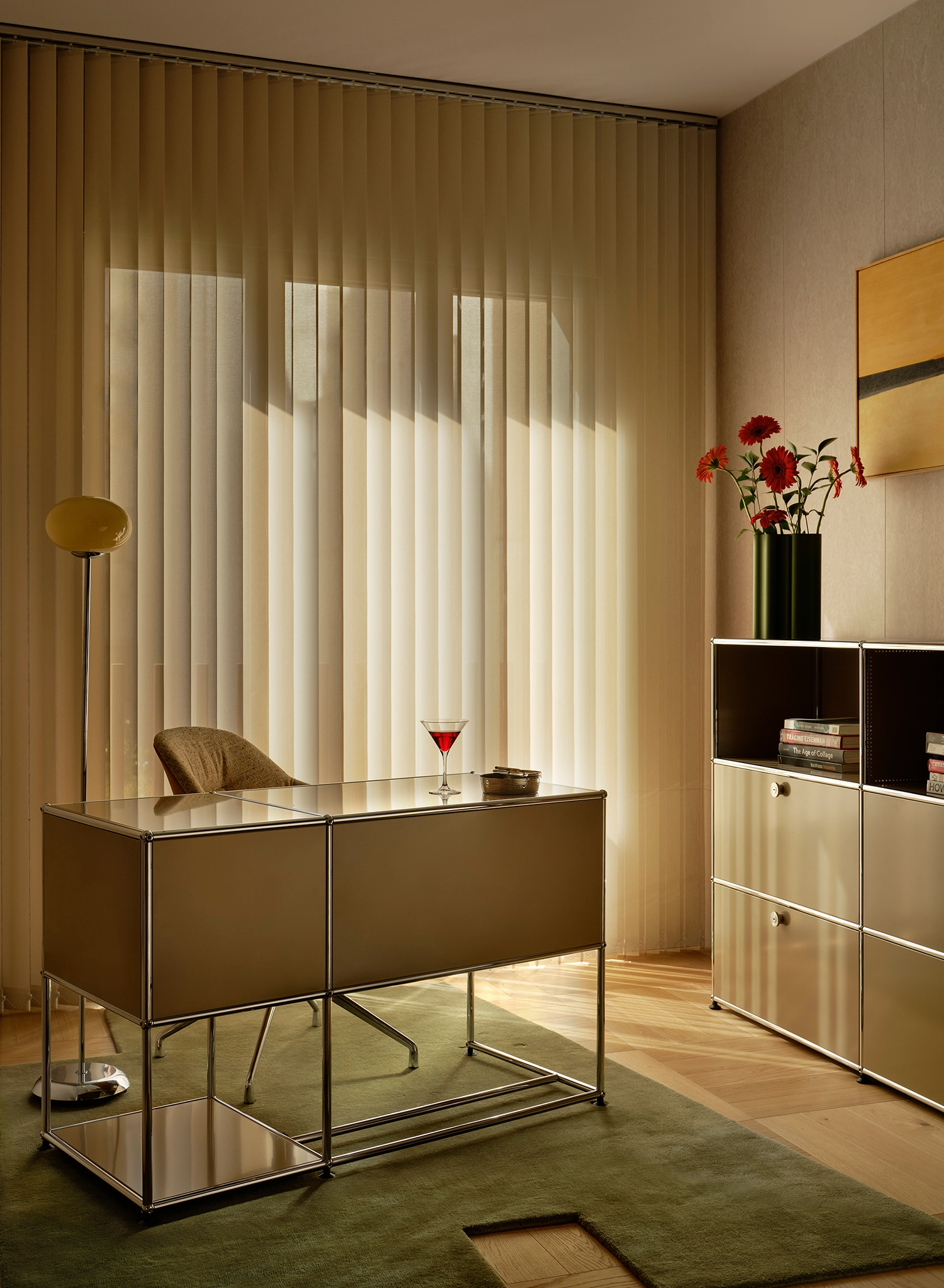 Minimalist home office with a USM Haller desk, green rug, and vertical blinds filtering sunlight.