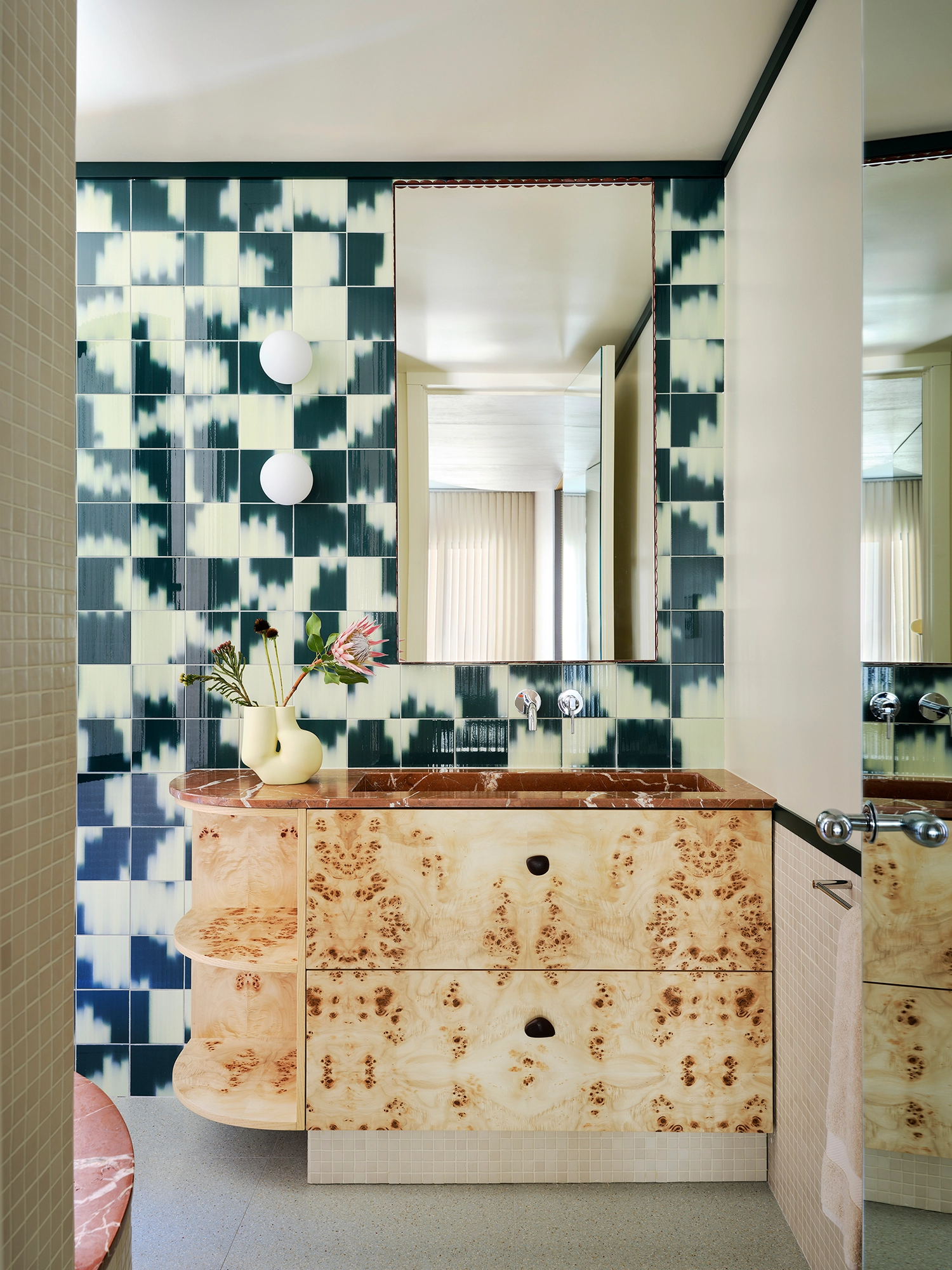 Bathroom vanity with a burr wood cabinet, red marble sink, and green and white patterned wall tiles.
