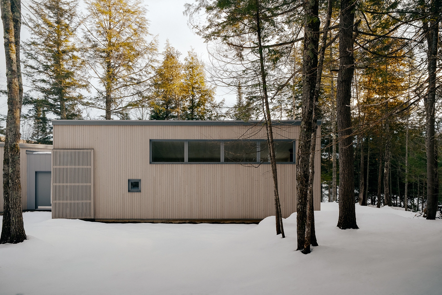 Elevation view of the vertical timber facade of Maison du Lac Perdu in a snowy landscape.