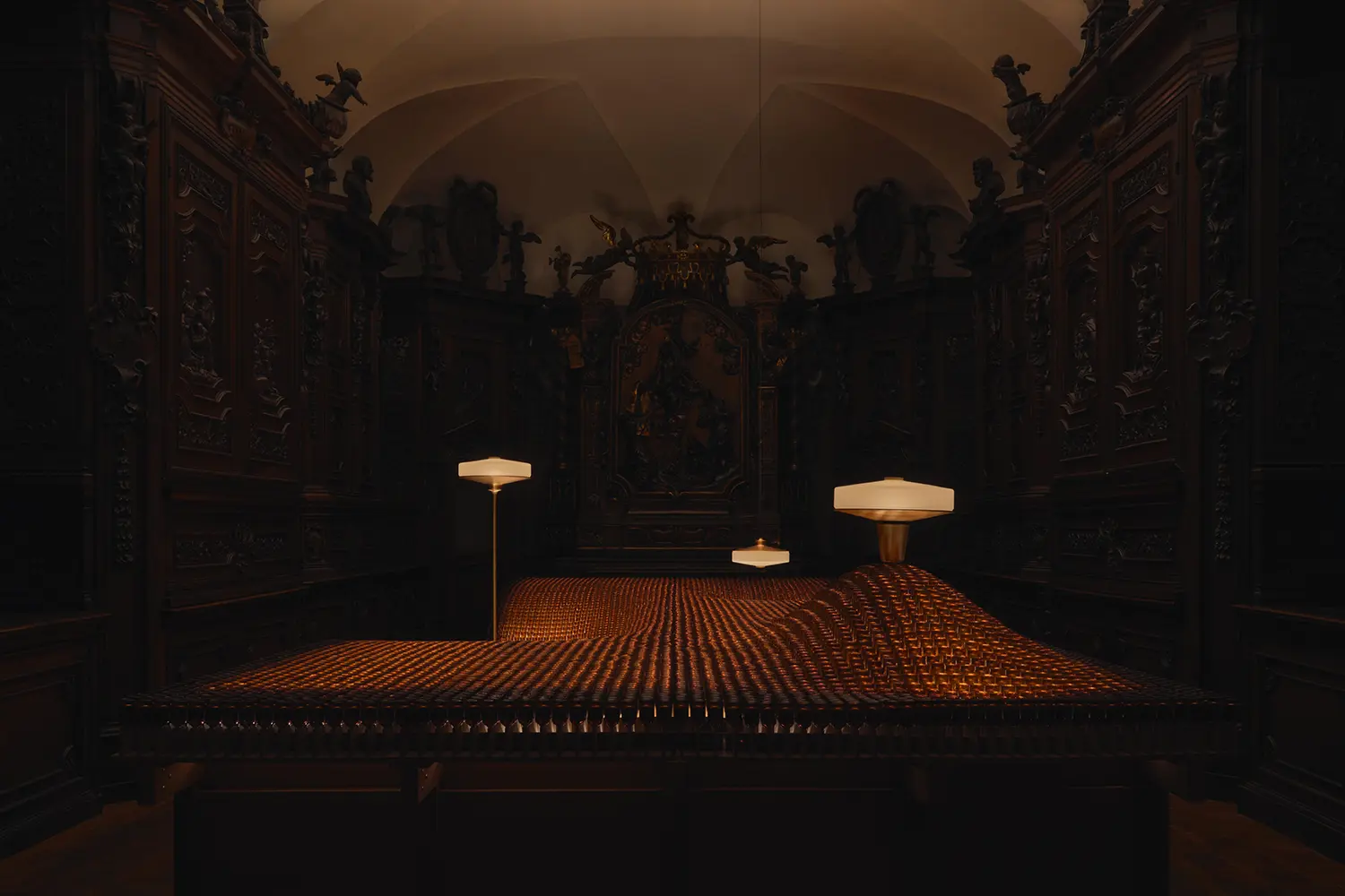 A wide shot of the sacristy with a glowing undulating wave of amber glass bottles topped by Aposē lamps.