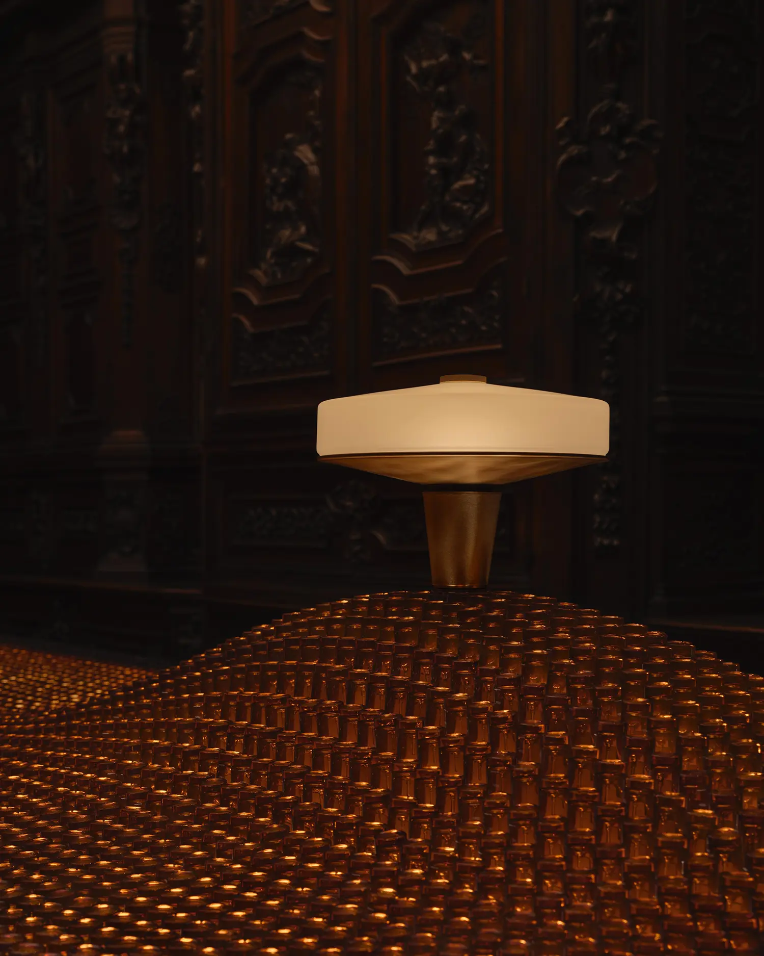 Close-up of the Aposē table lamp resting on a sea of amber fragrance bottles in a dark, historic room.