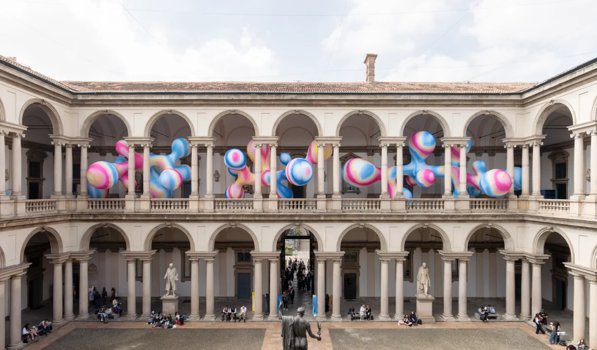 Wide shot of the Pinacoteca di Brera courtyard featuring multi-colored inflatable structures along the upper loggia.