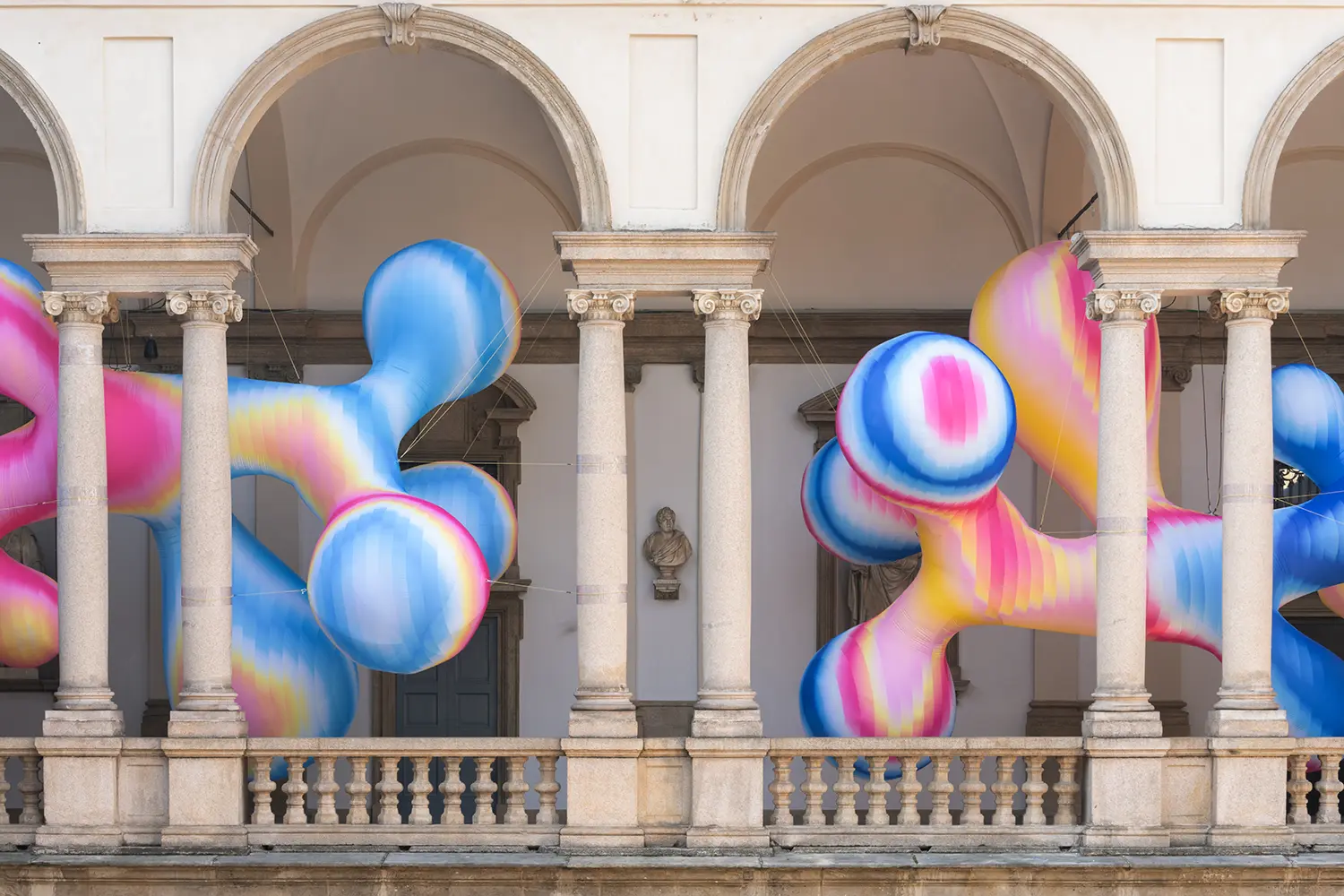 Close-up of blue, pink, and yellow inflatable spheres nestled between the classical columns of the Brera loggia.