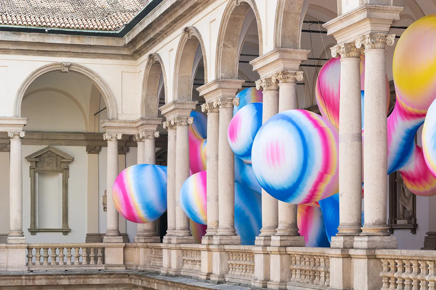 Side perspective of the upper gallery at Pinacoteca di Brera with large, spherical inflatable art pieces.
