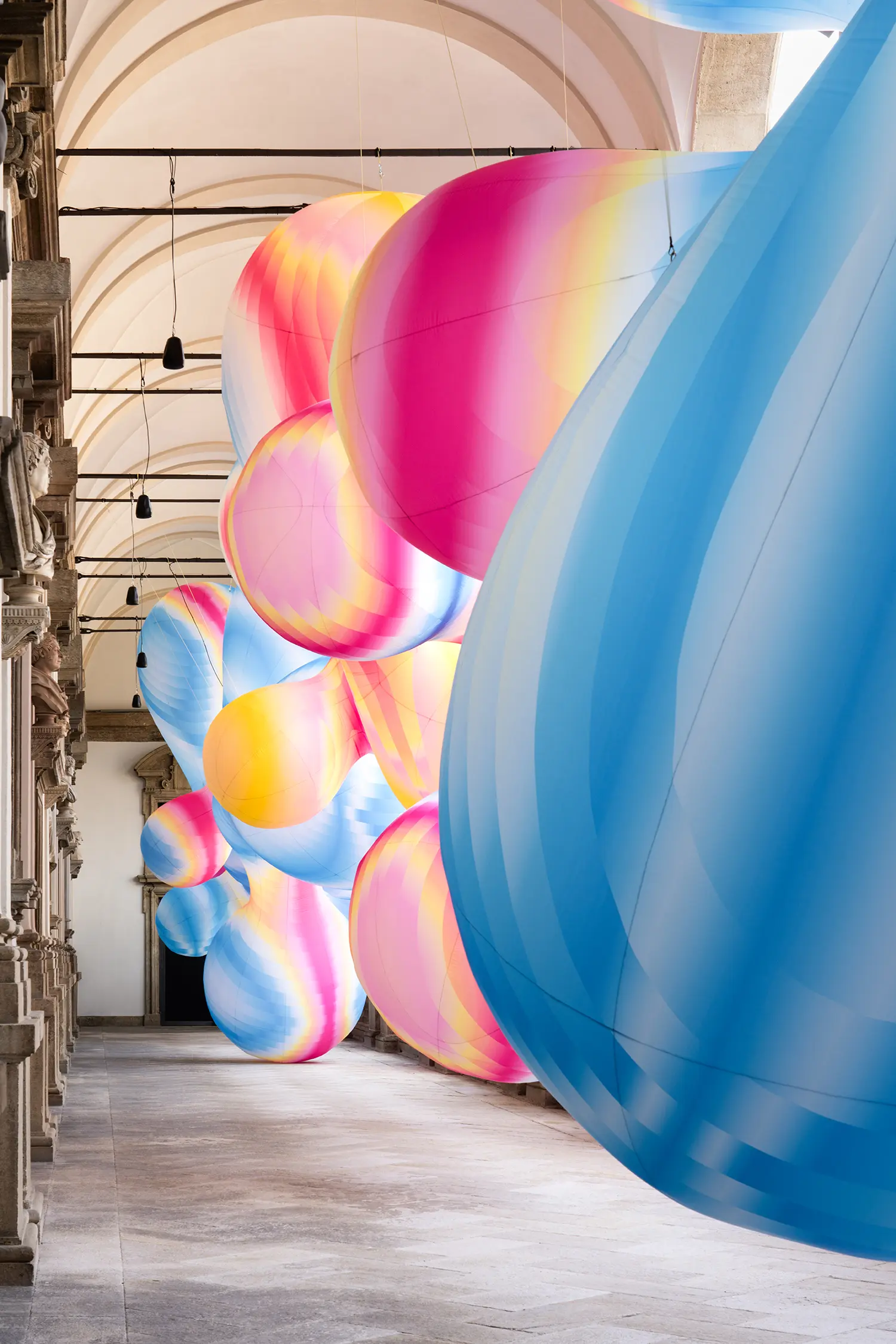 Interior view of a corridor filled with suspended, colorful inflatable shapes in blue and magenta tones.