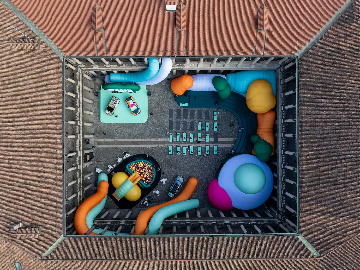 An aerial drone shot of the Palazzo del Senato courtyard filled with colorful inflatable tubes, spheres, and yoga mats arranged in a circular pattern.