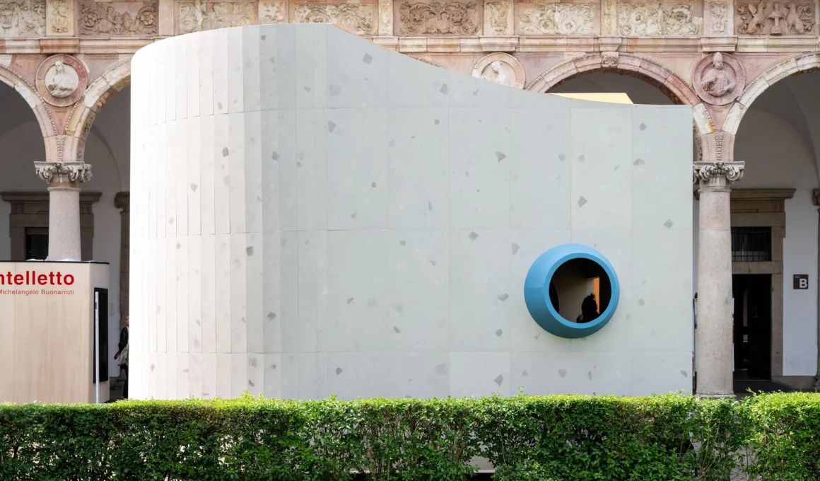 Close-up view of the curving grey textured facade with a prominent blue-ringed porthole.