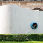 Close-up view of the curving grey textured facade with a prominent blue-ringed porthole.