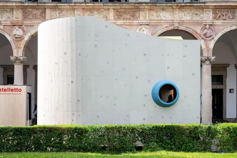 Close-up view of the curving grey textured facade with a prominent blue-ringed porthole.
