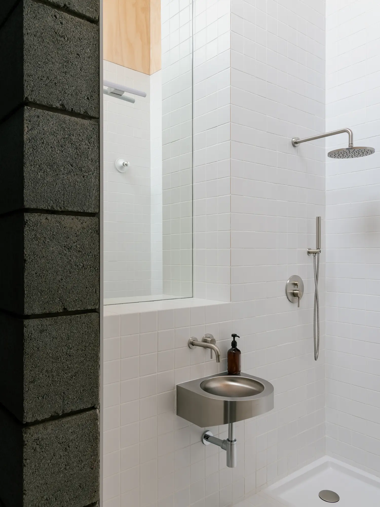 Detail of a minimalist bathroom with a small stainless steel sink and white square tiles.