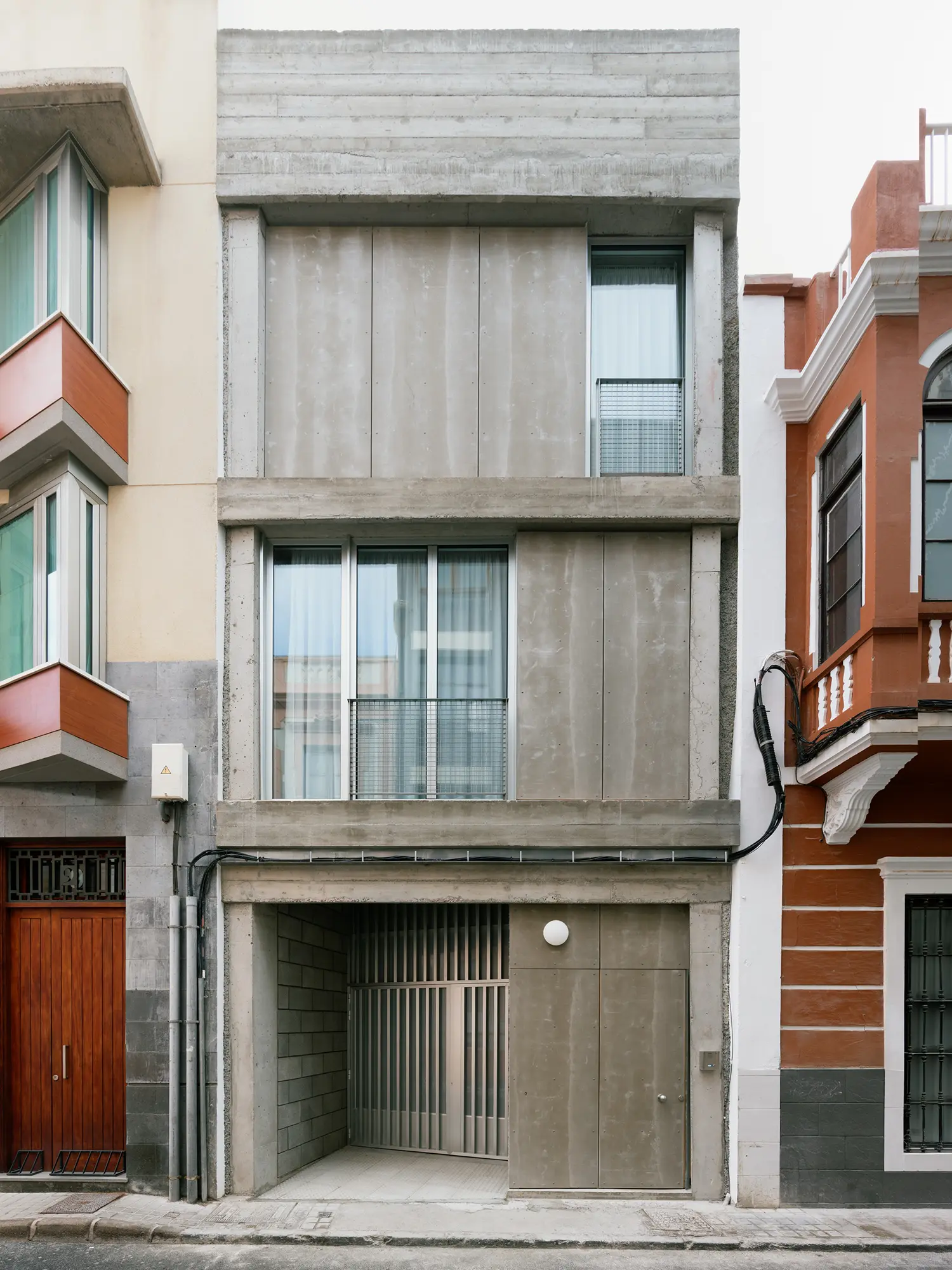 Narrow three-story facade of Casa Iriarte in Las Palmas with raw concrete and vertical cement panels.