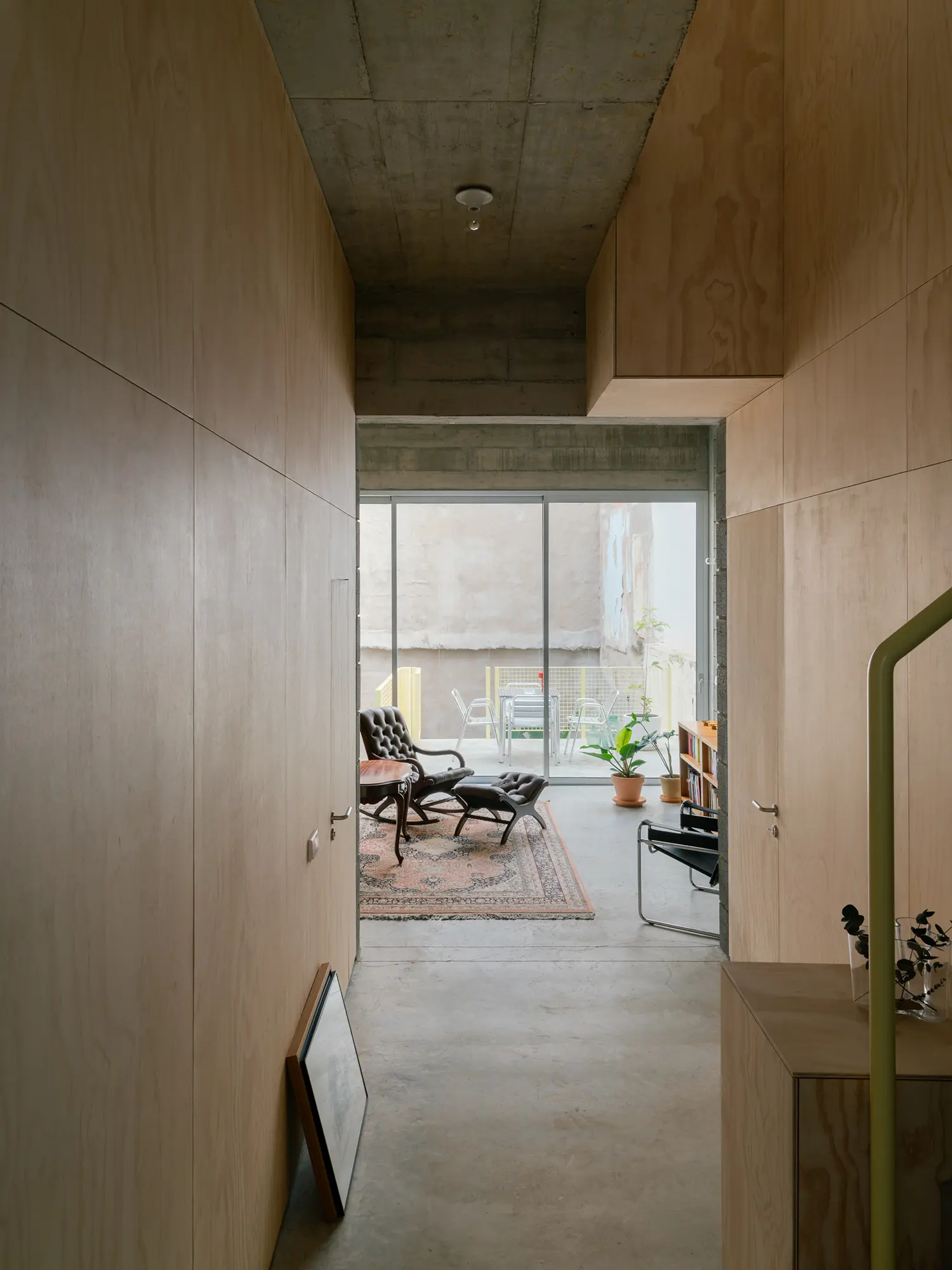 Long perspective through a timber-lined corridor leading to a bright living area with a patio view.