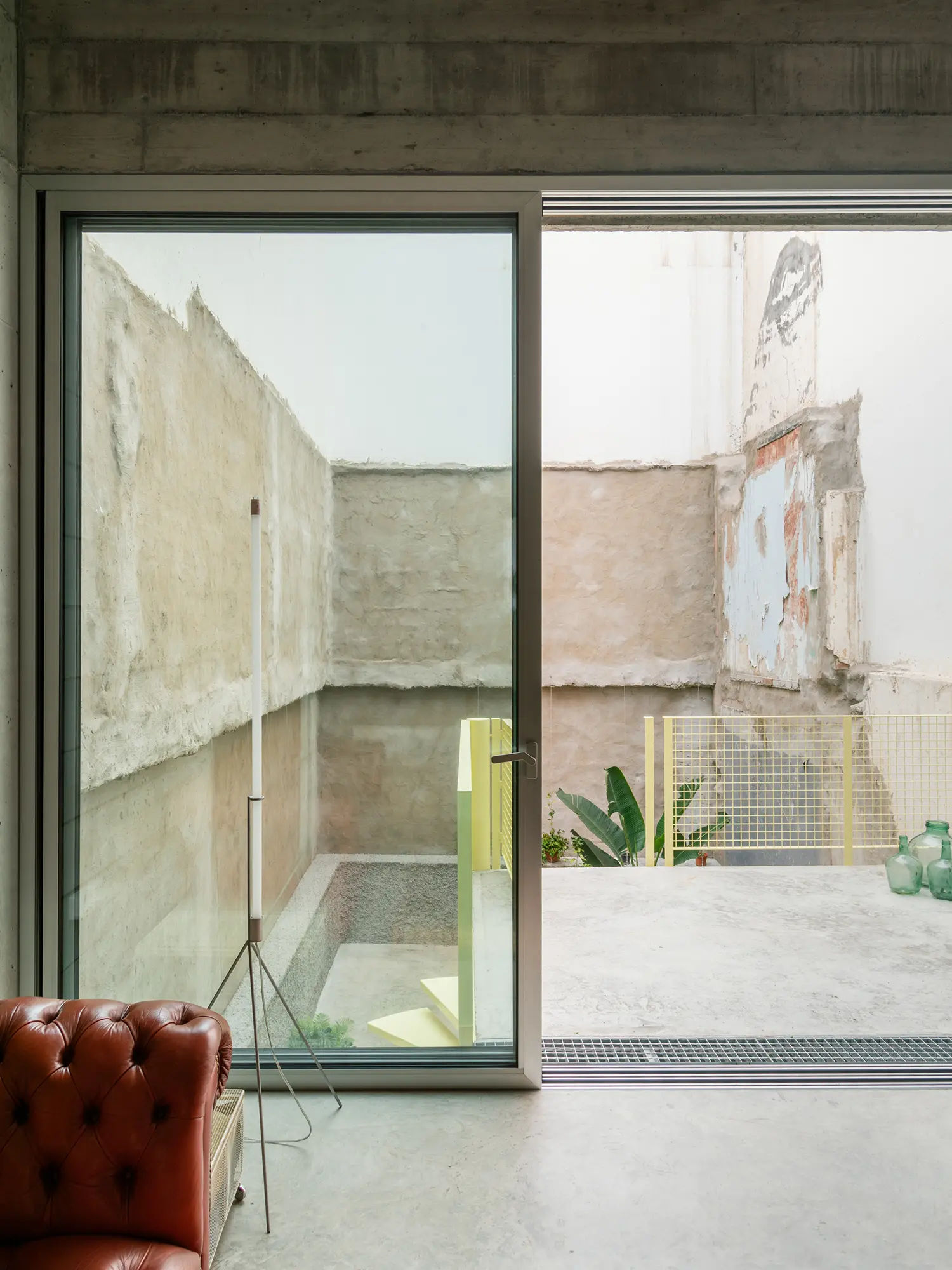 Sliding glass door opening onto a concrete terrace with a yellow metal railing and a leather sofa in the foreground.