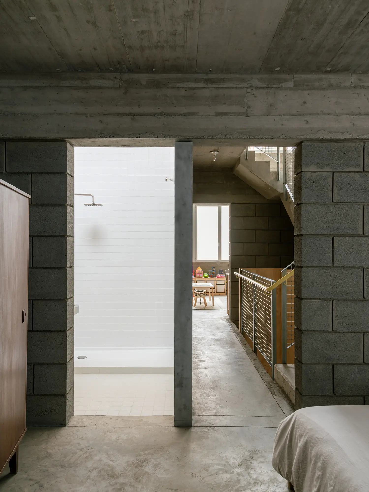Minimalist bathroom entrance with white tiles and a stainless steel shower head next to volcanic blocks.