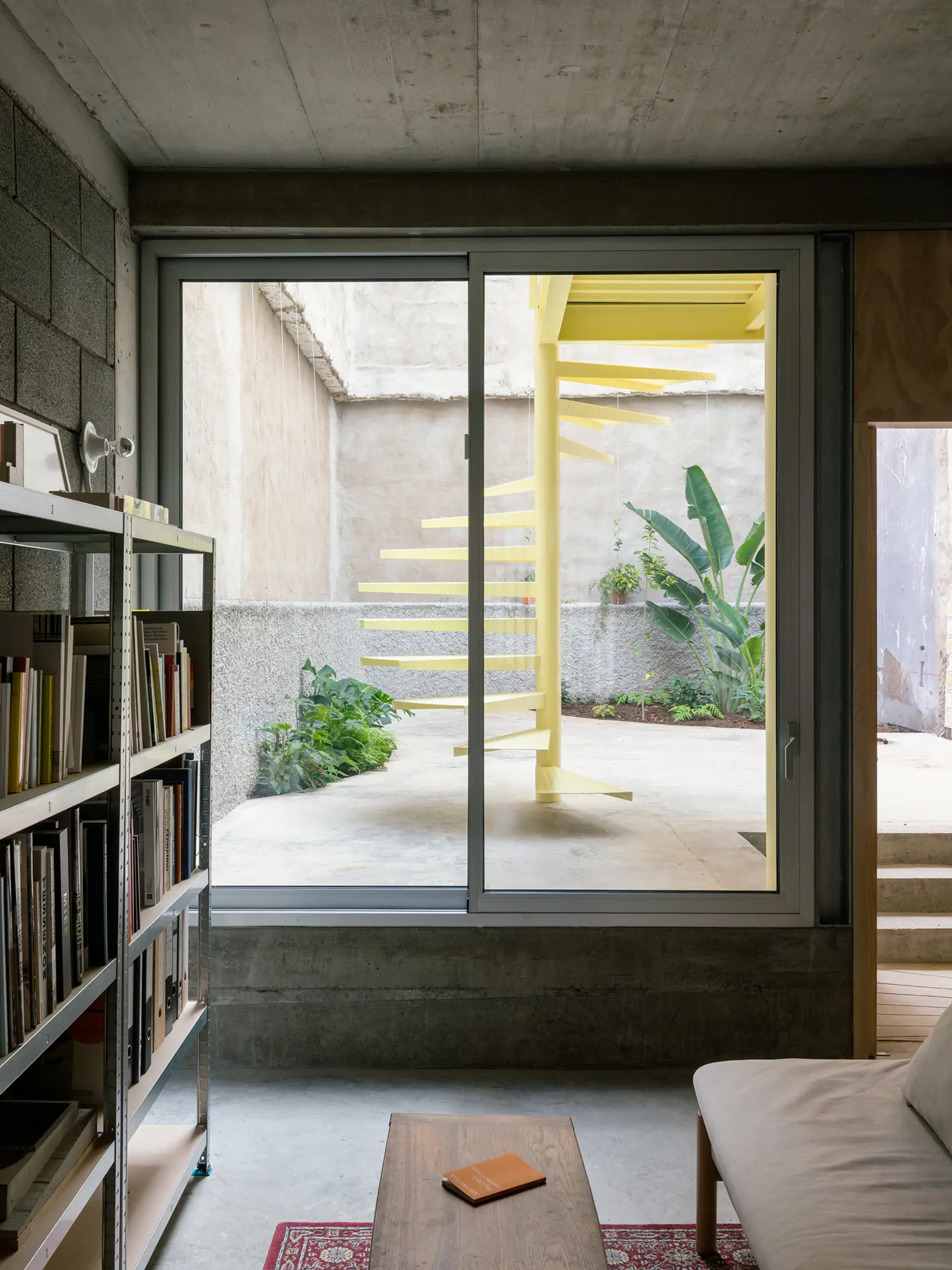 View from a library or studio space through a window toward a yellow spiral staircase in a courtyard.
