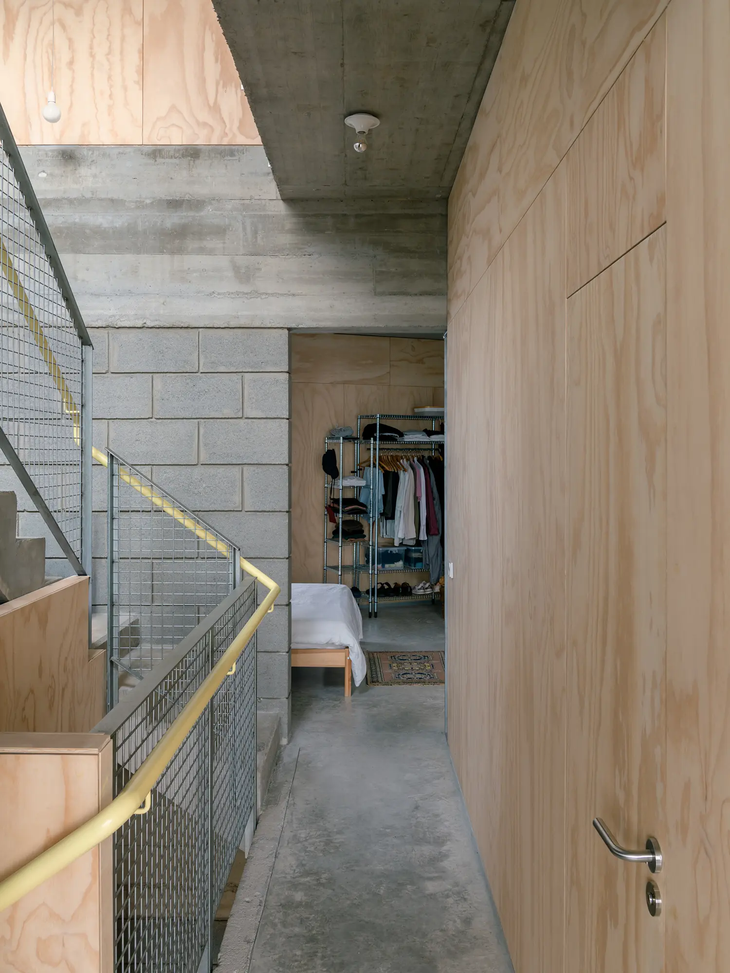 Plywood hallway in Casa Iriarte with a view of a bedroom and a metal mesh staircase railing.