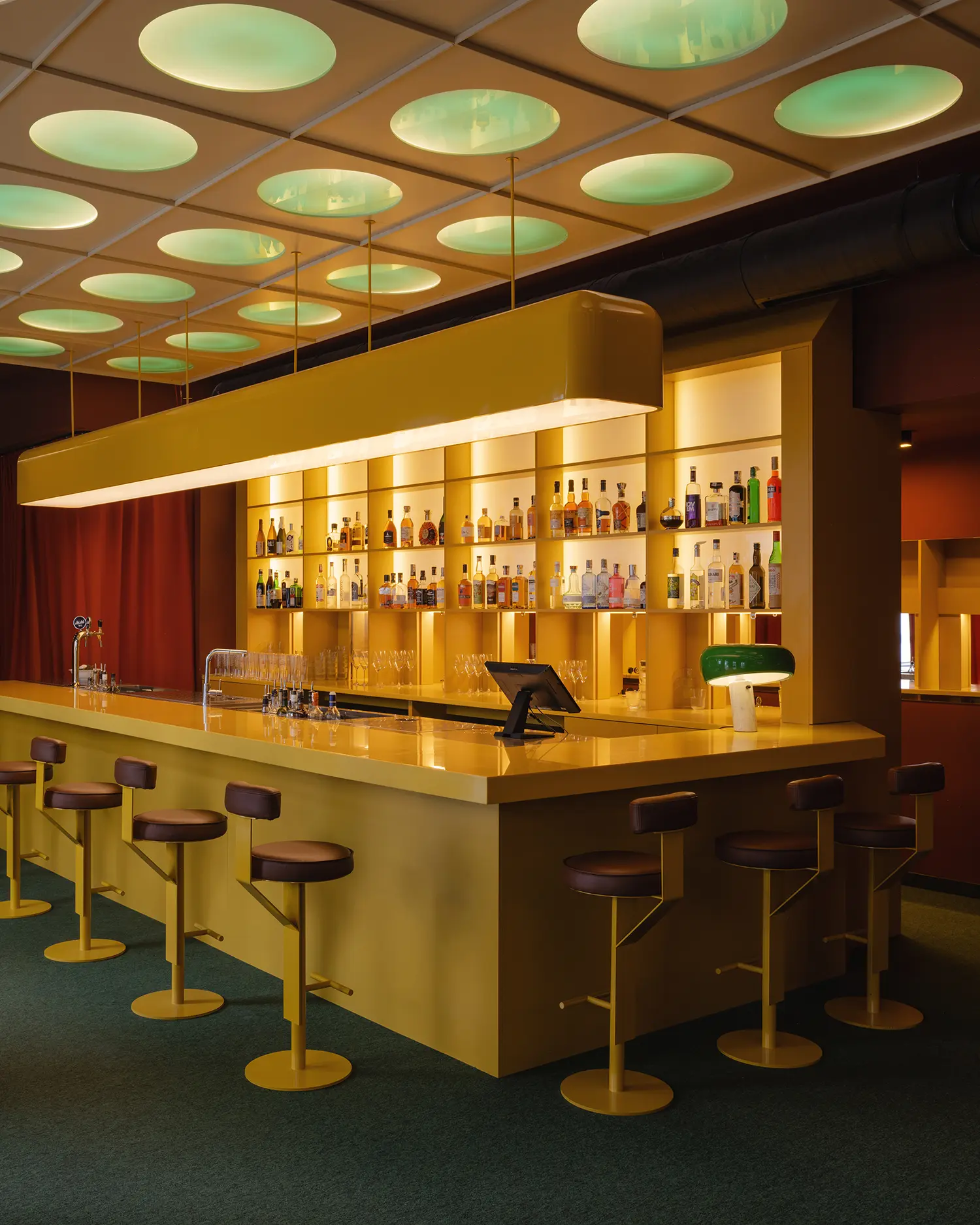 Modern bar counter at EJE with illuminated shelves and a green table lamp.