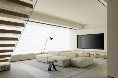 Minimalist living room with modular off-white sofa and floating wooden staircase.