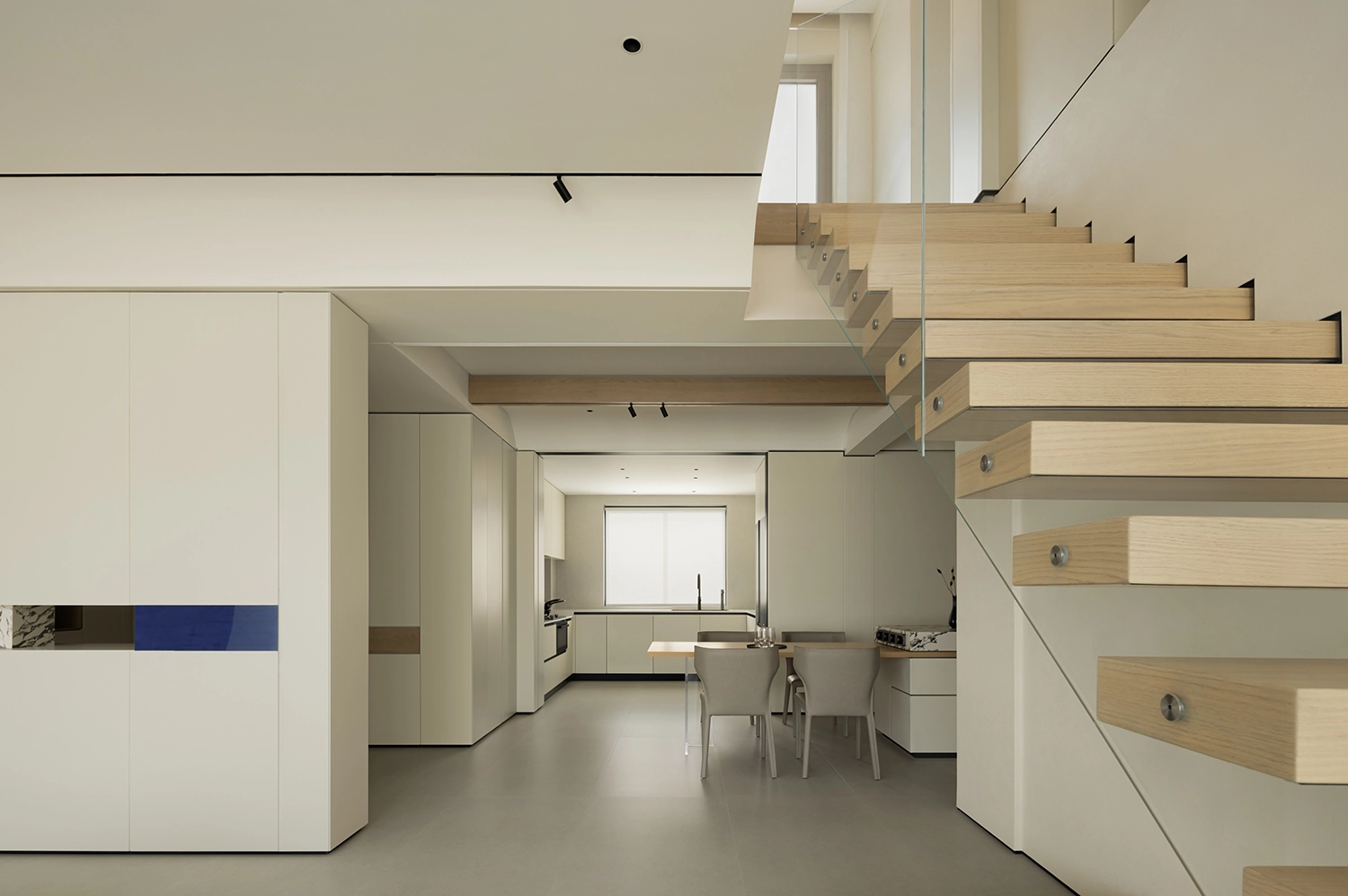 Floating wooden staircase with glass guardrails overlooking a minimalist kitchen and dining area.