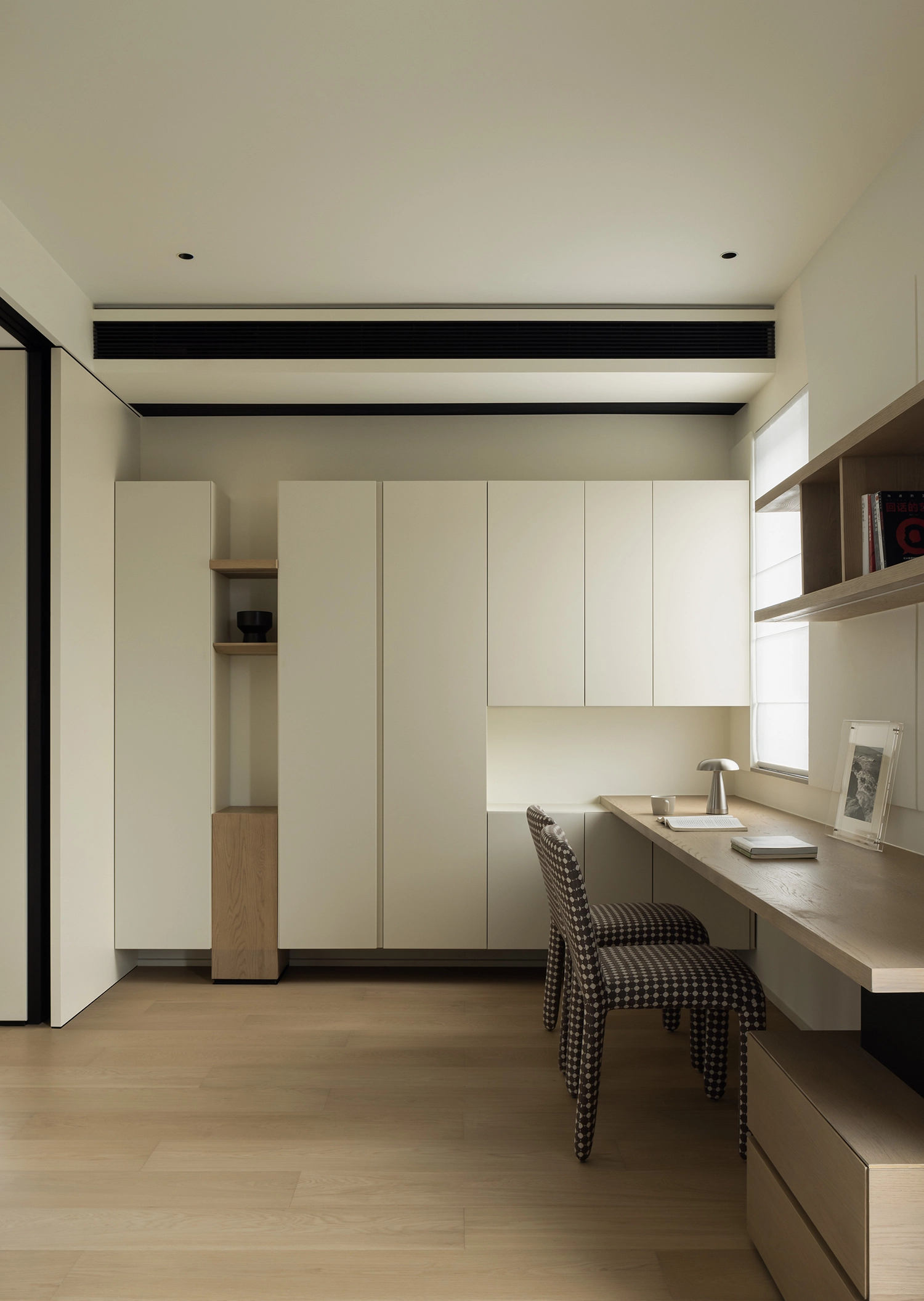Minimalist home office with long wooden desk and built-in off-white shelving.