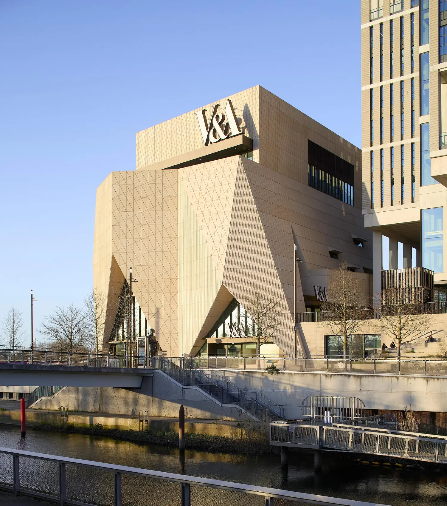 The V&A East Museum viewed from the canal, highlighting its towering, pleated concrete form.