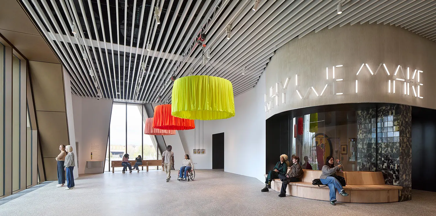 Interior of the V&A East Museum lobby featuring "Why We Make" neon signage and colorful hanging installations.