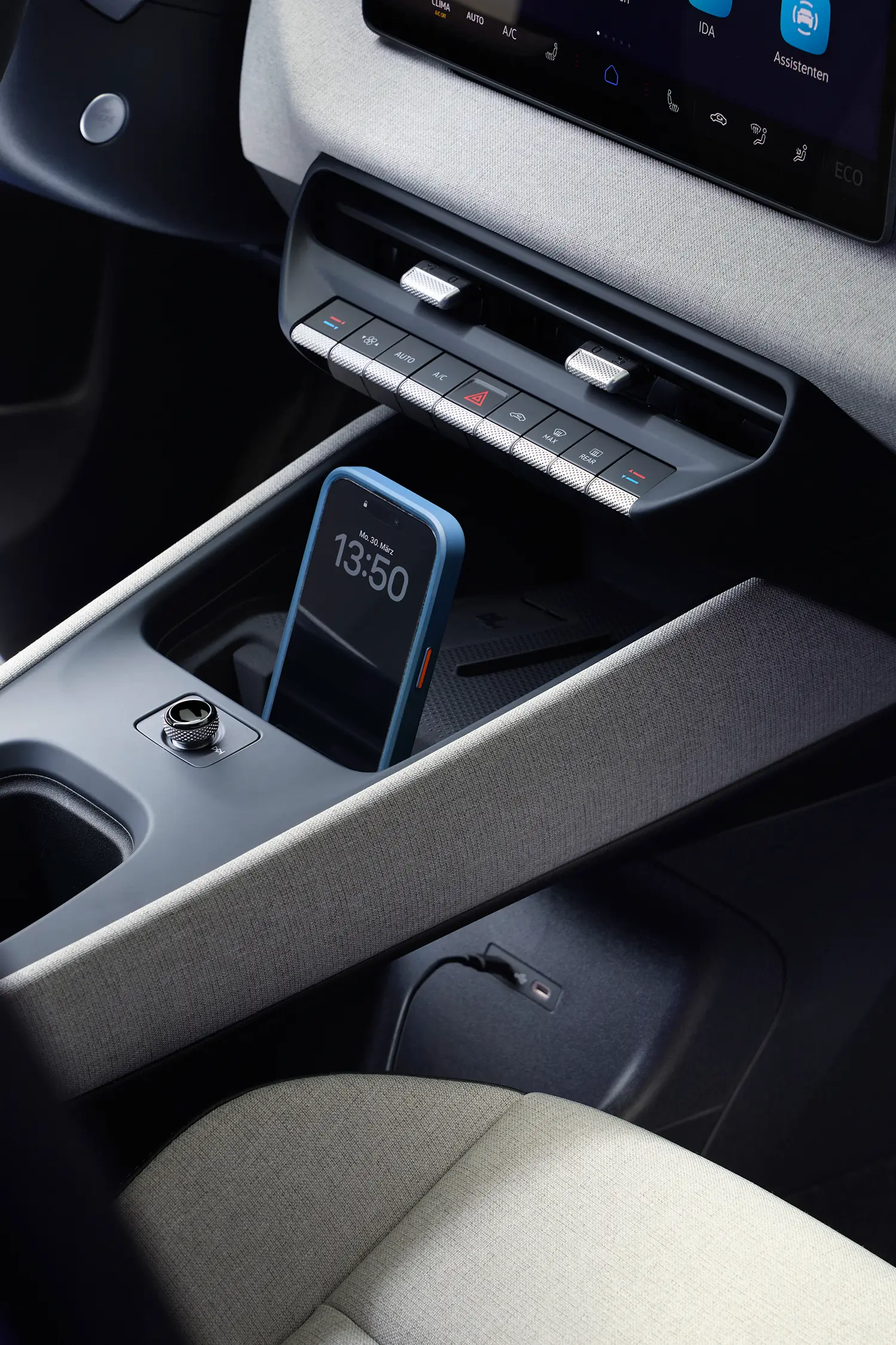 Close-up of the center console showing physical climate controls and a smartphone.