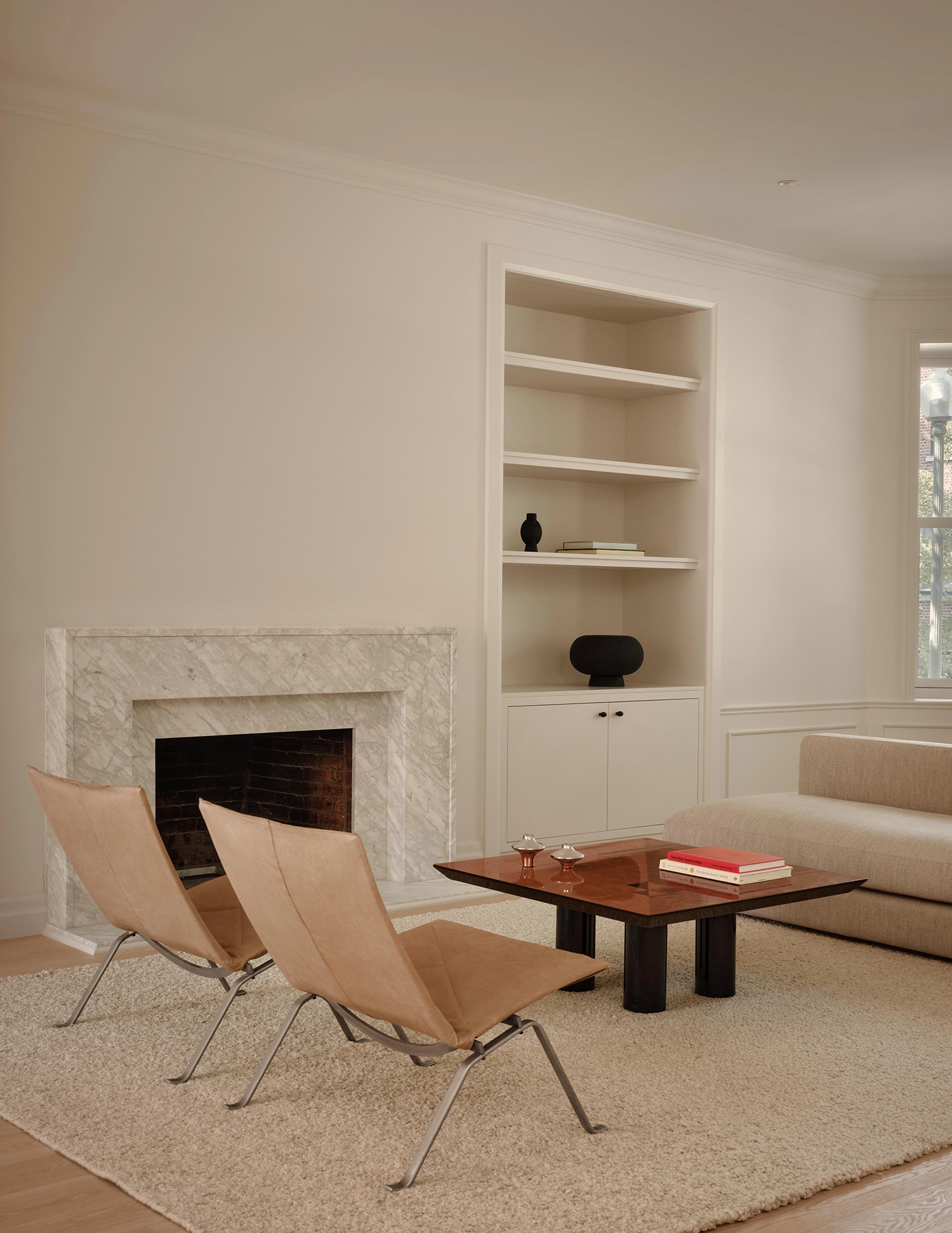 A living room corner featuring a white marble fireplace, a built-in bookshelf, two tan leather lounge chairs, and a dark wood coffee table.