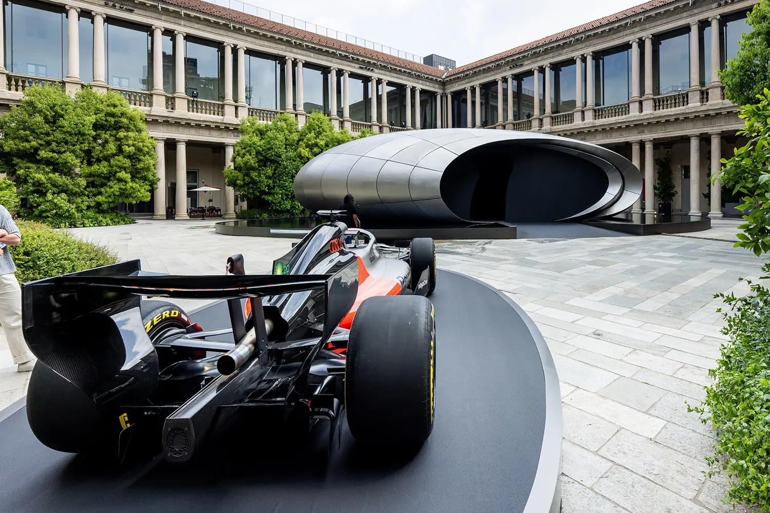 Rear view of the Audi R26 Formula 1 car on a circular podium, positioned in front of the Zaha Hadid Architects Origin pavilion.