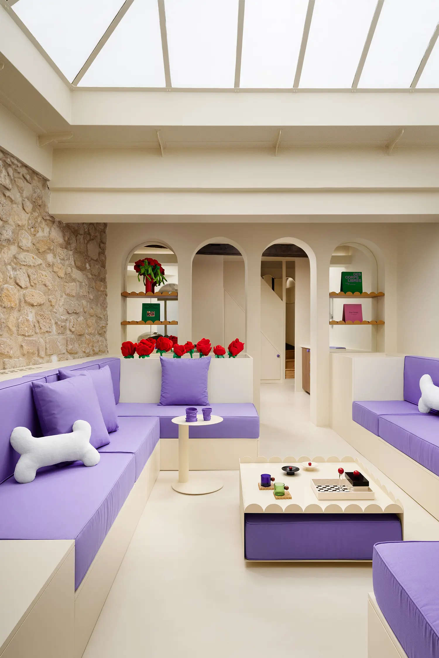 Sunken lounge area with bone-shaped pillows and a scalloped white coffee table under a glass roof.