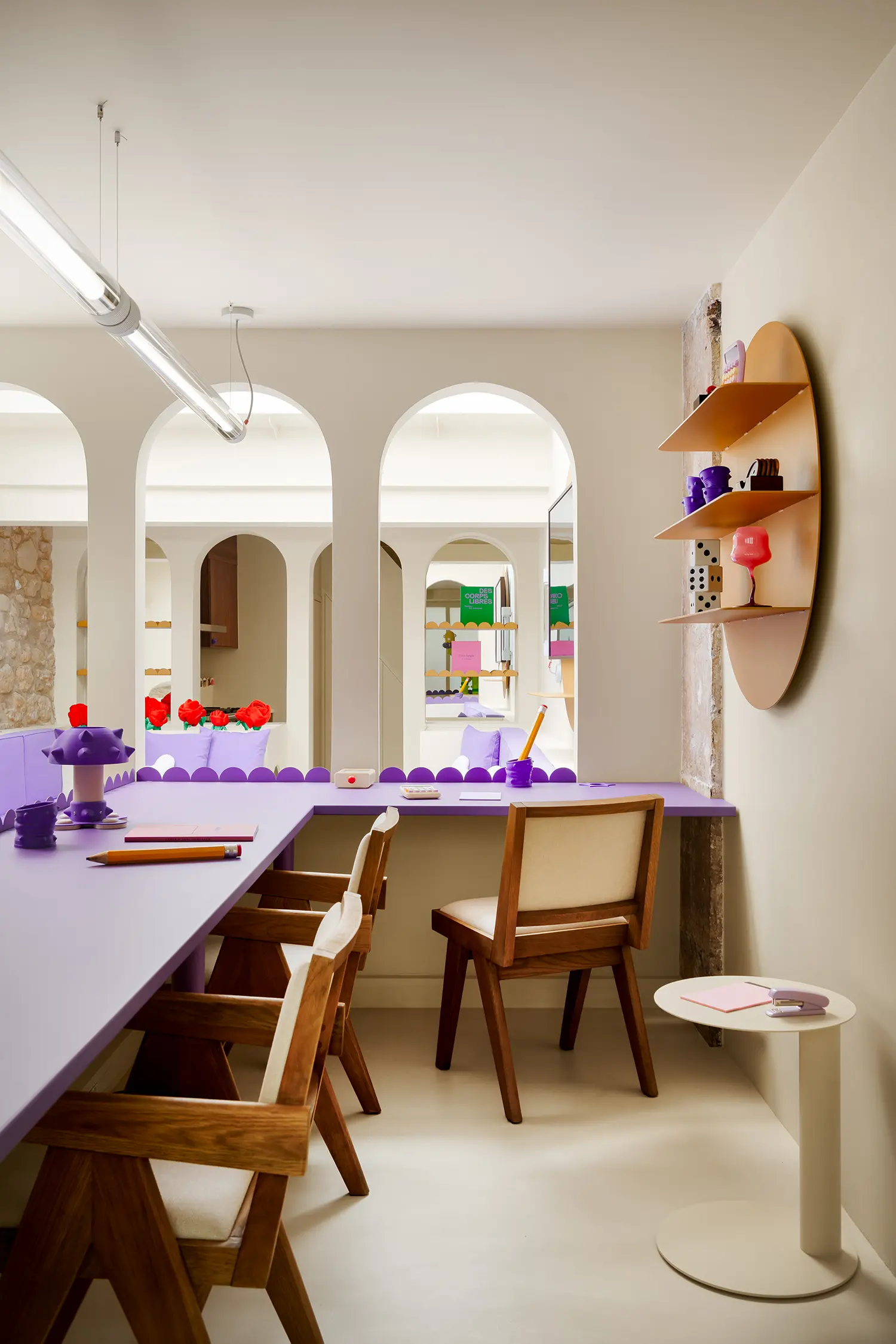 Individual workspace with wooden chairs, L-shaped purple desks, and circular shelving units.