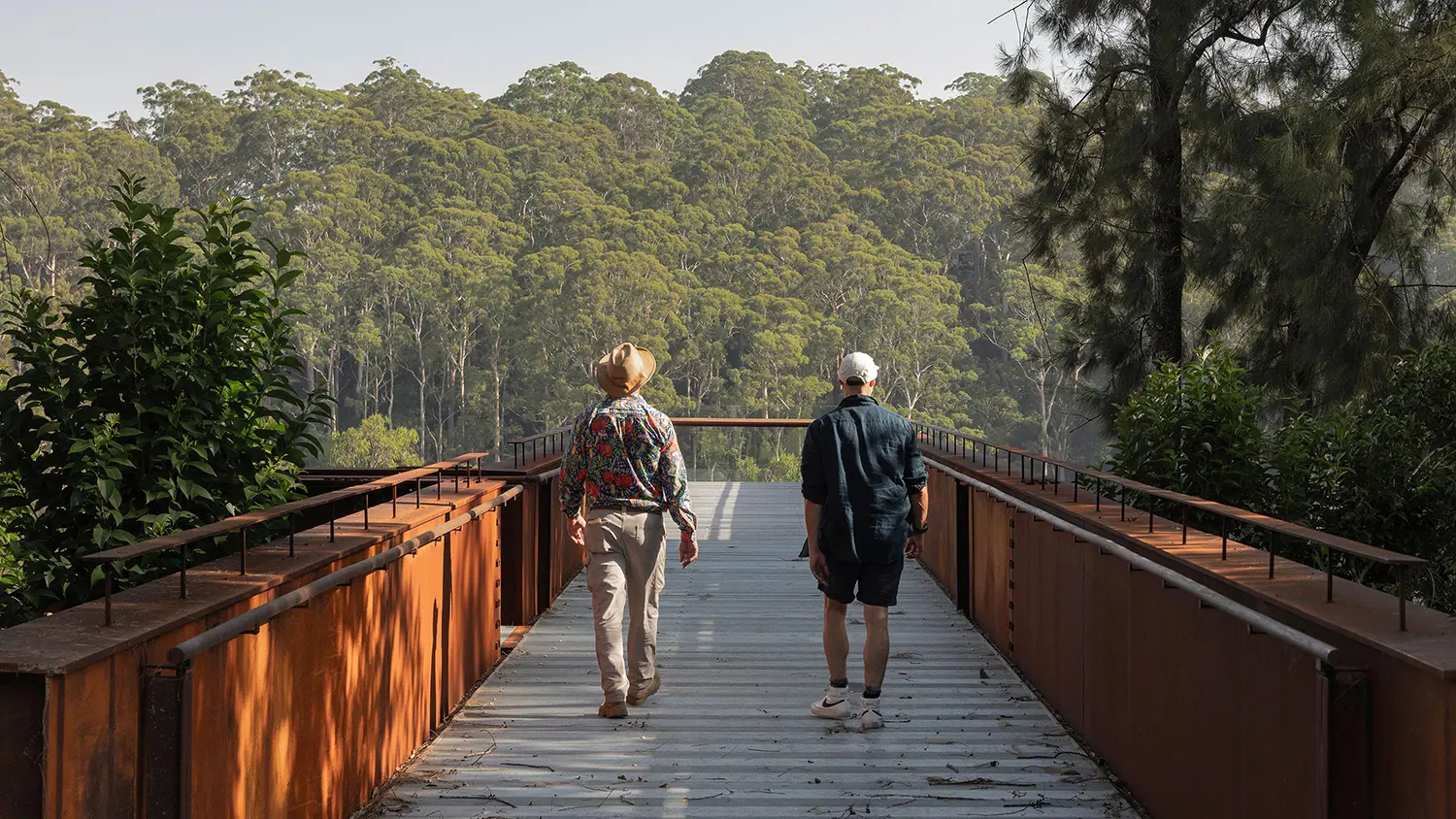 Visitors walking along the industrial steel walkway of the Southern Lookout toward a horizon of dense eucalyptus forest.