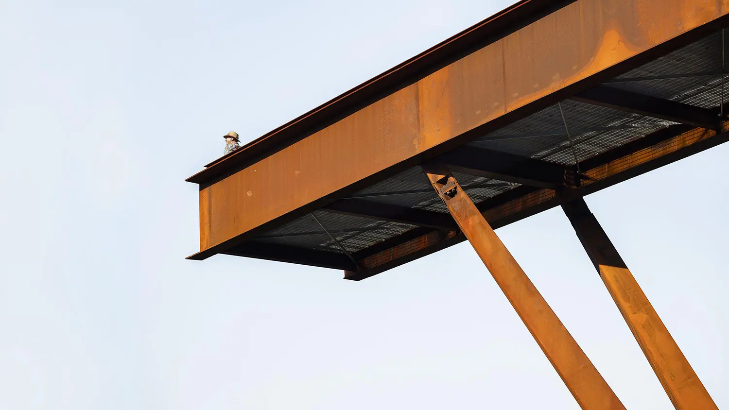 Detailed shot of the rusted steel I-beam at the tip of the lookout cantilever with a visitor visible behind the safety railing.