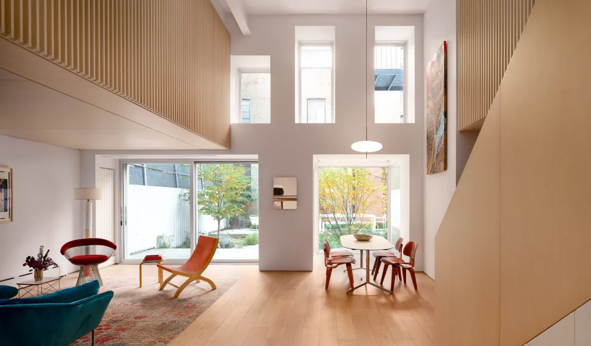 Open-plan living room in a Manhattan apartment featuring a double-height ceiling, white oak flooring, and large glass doors opening to a private garden.