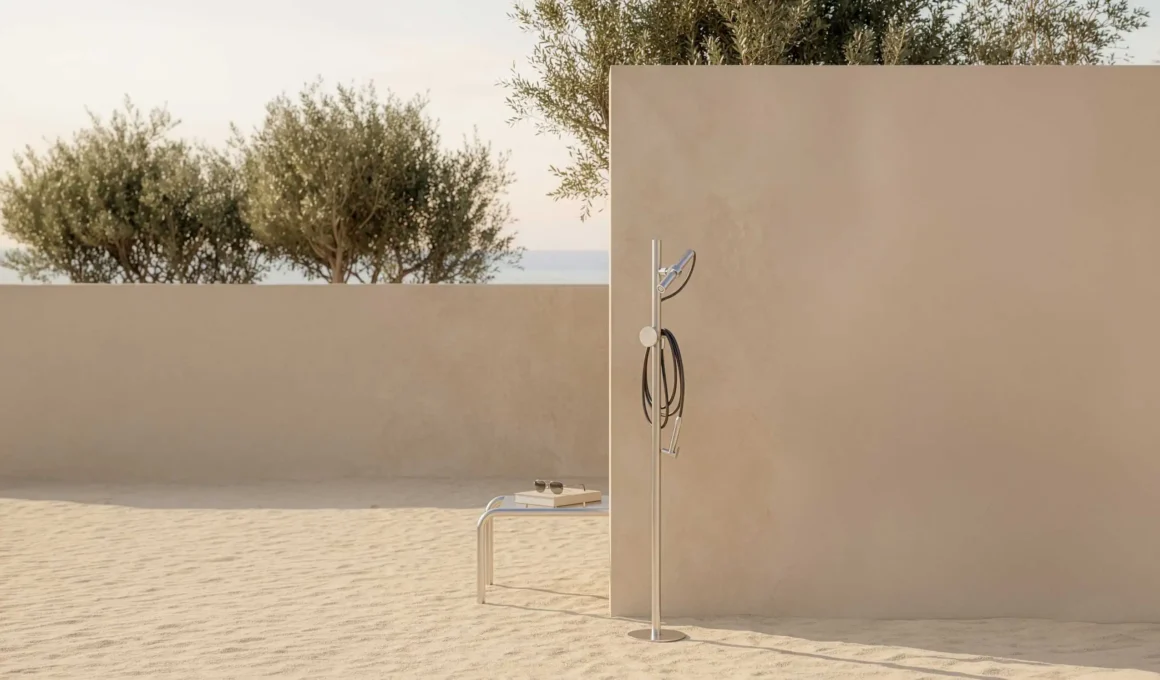 Minimalist outdoor shower system FormaLibera by We Are IB designed by Pierattelli Architetture featuring a stainless steel finish against a textured masonry wall and Mediterranean landscape.