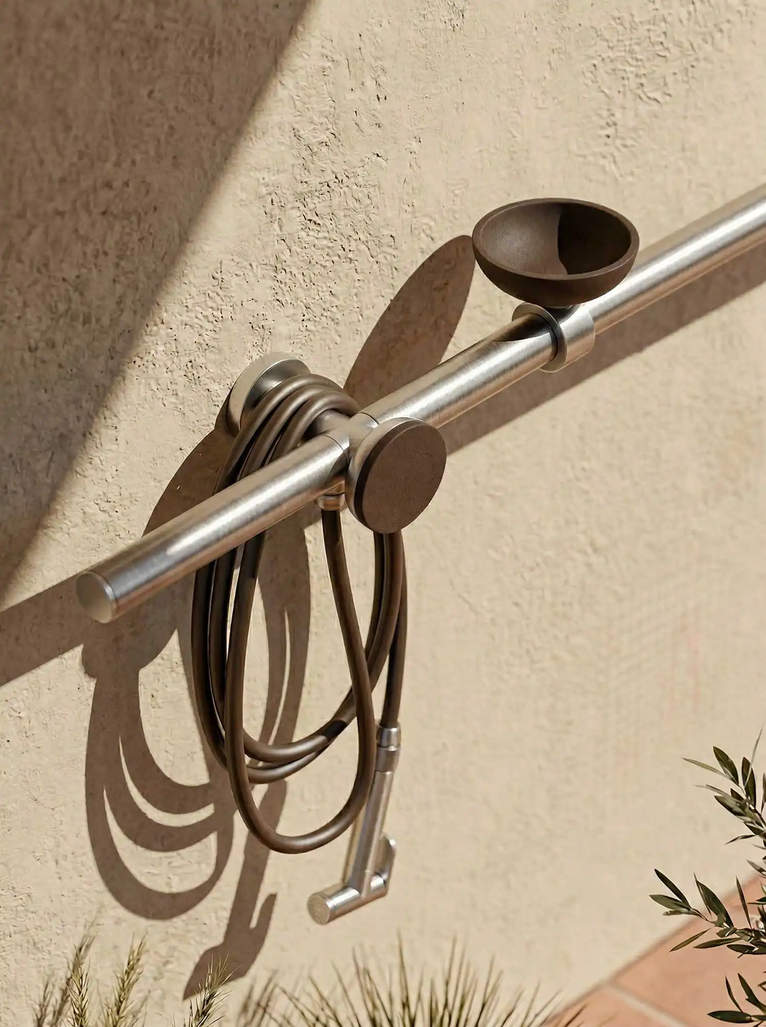 Close-up technical detail of the FormaLibera outdoor shower controls and flexible hose by We Are IB, showcasing raw metallic finishes and tactile masonry texture.