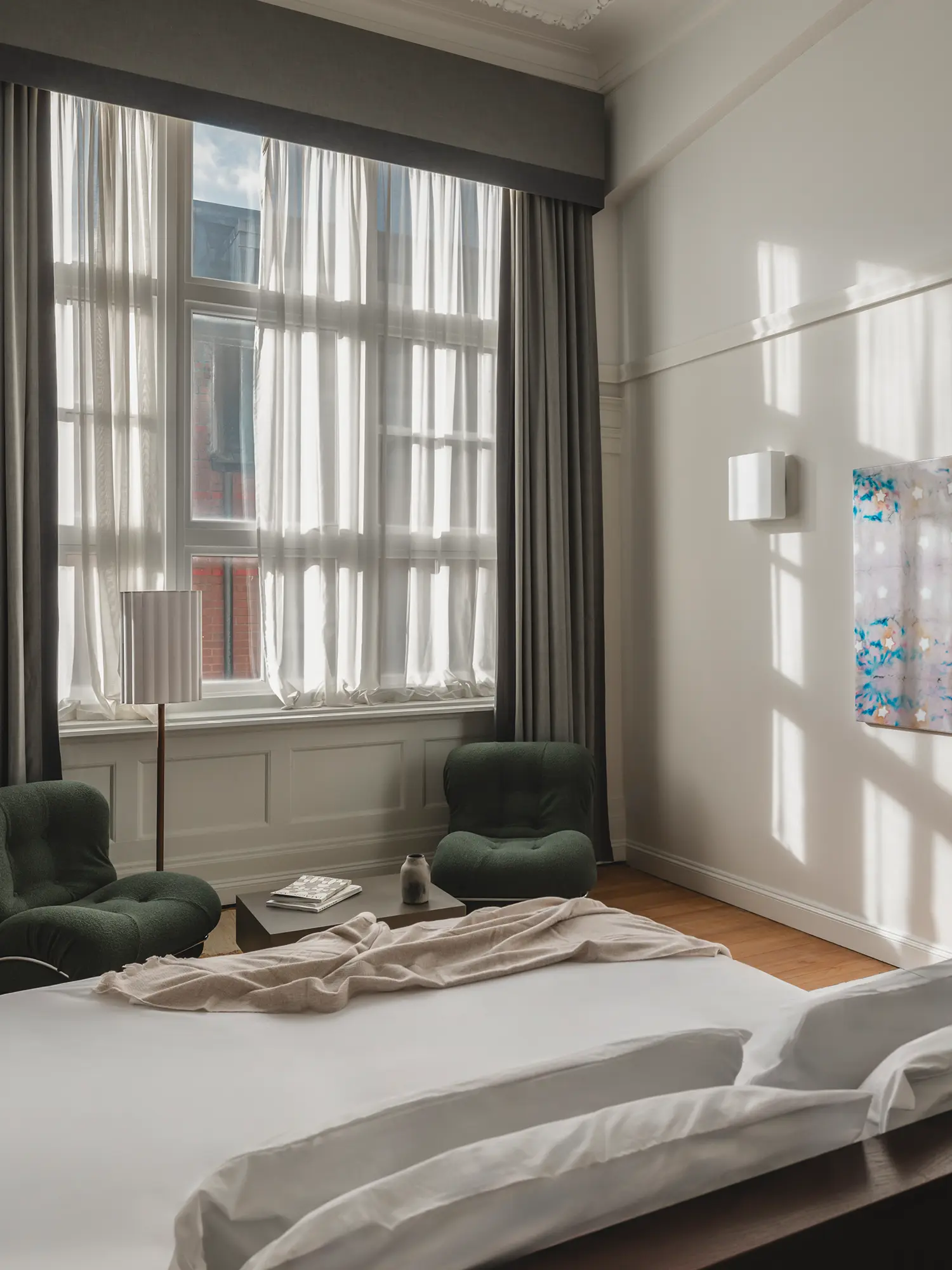 Sunlit guestroom at Arthouse Glasgow with green lounge chairs and high ceilings.