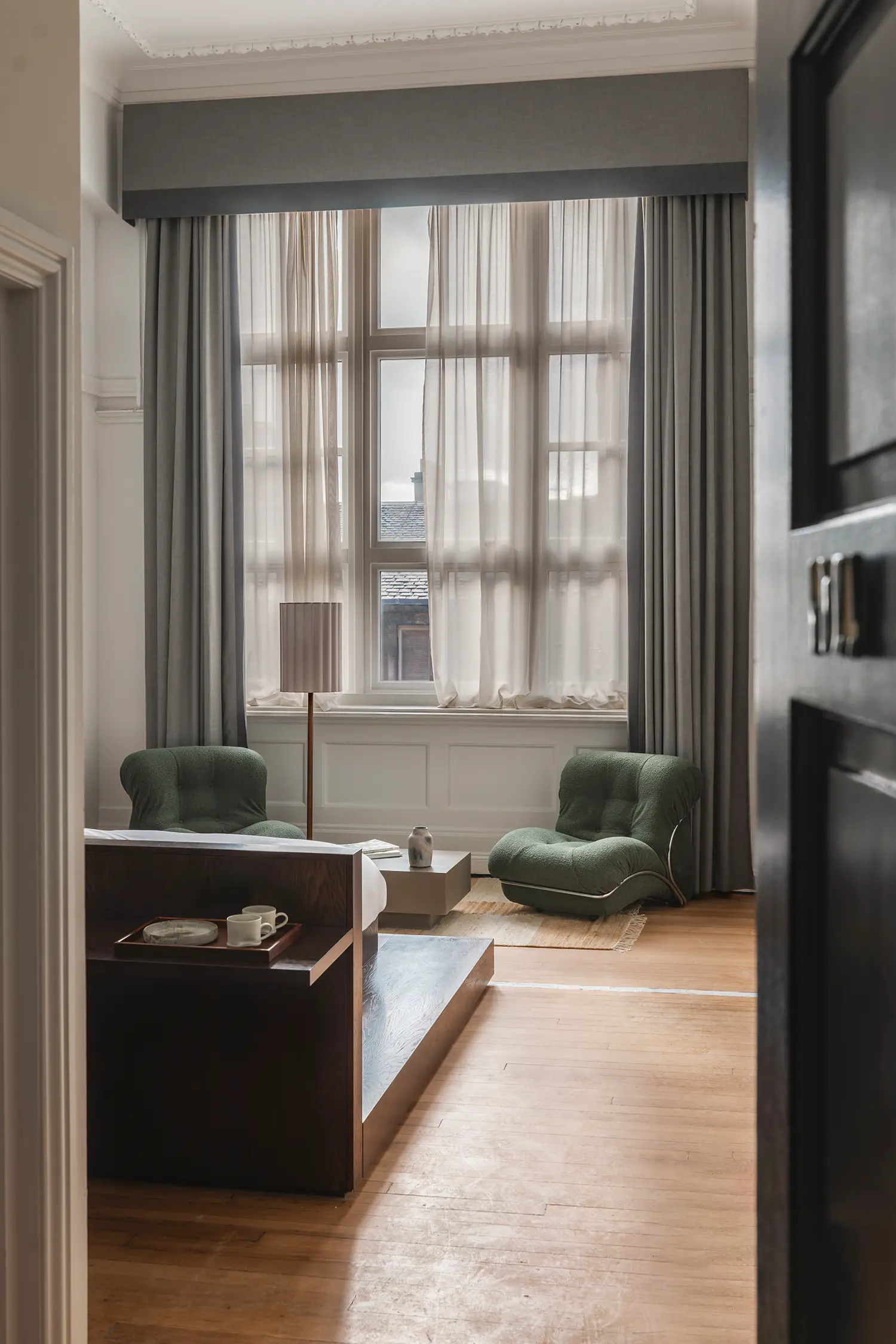 View into a hotel room at Arthouse Glasgow showing a wooden platform bed and large windows.