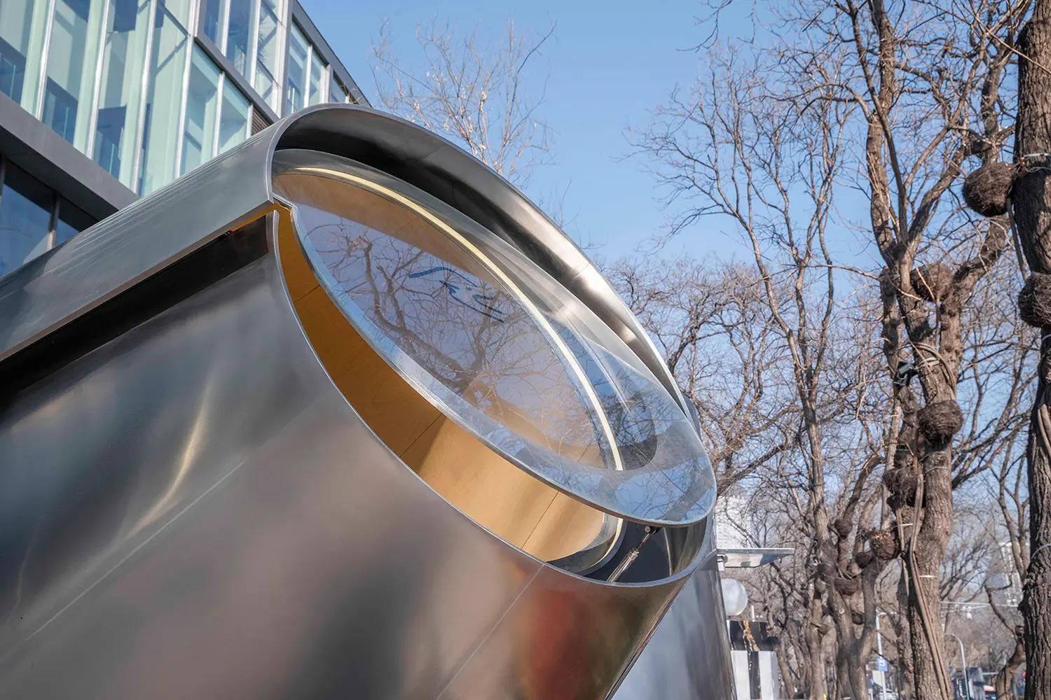 Close-up of the circular glass roof on the slanted metal volume against a clear blue sky.
