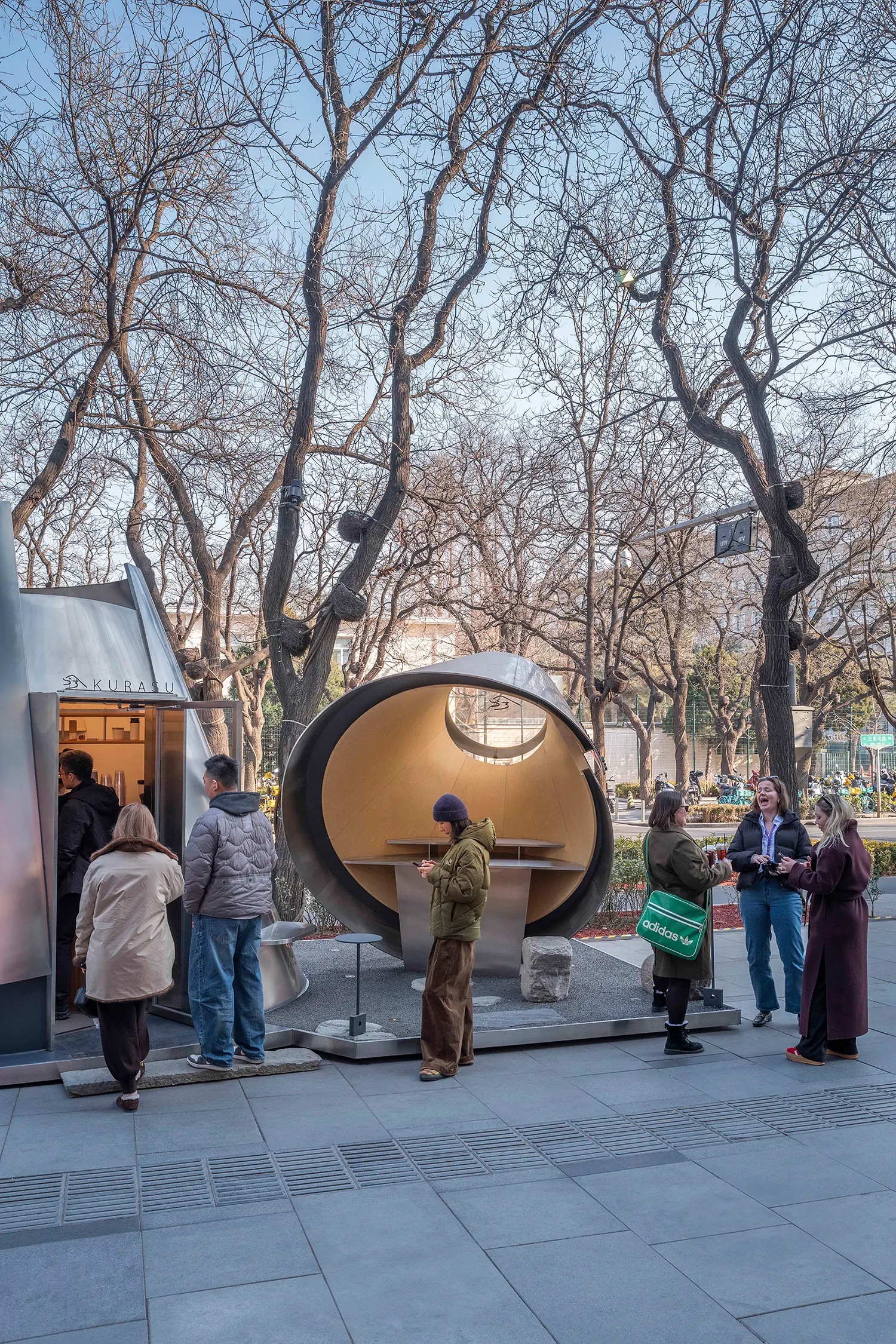 Pedestrians standing in line at the Kurasu pop-up entrance next to the open social volume.